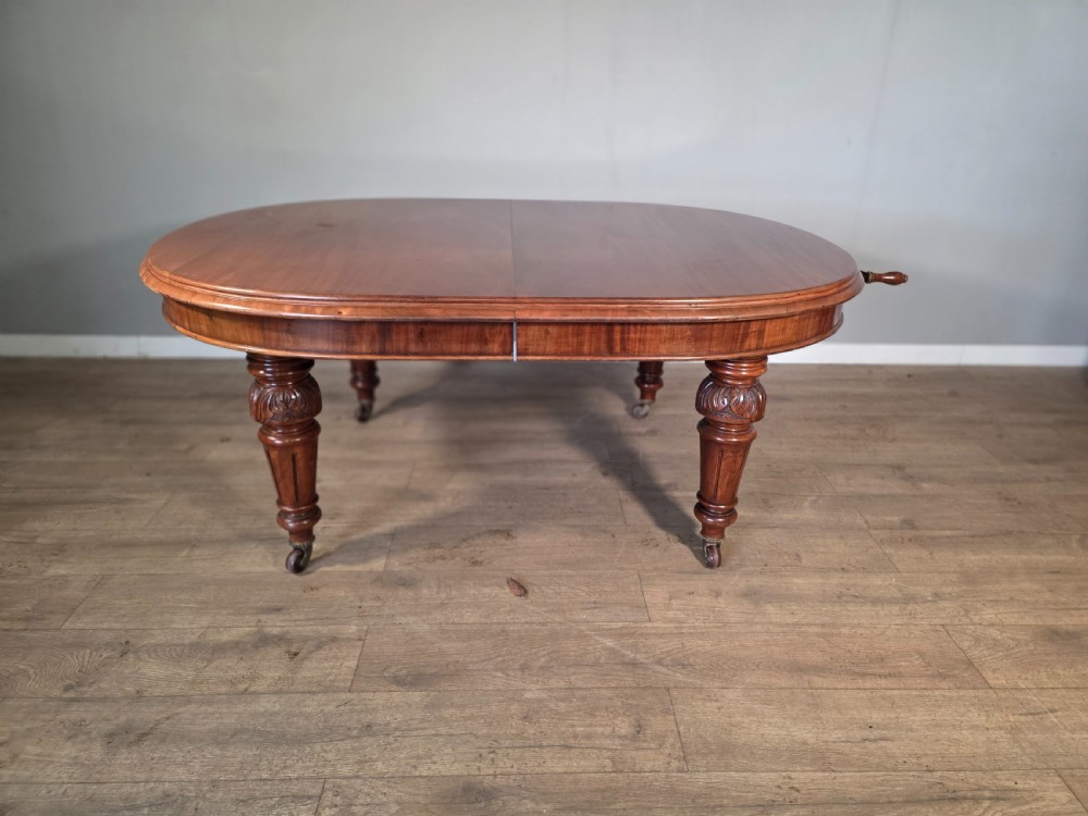 An antique Victorian mahogany extending dining table featuring an oval top, turned carved legs, and brass castors.