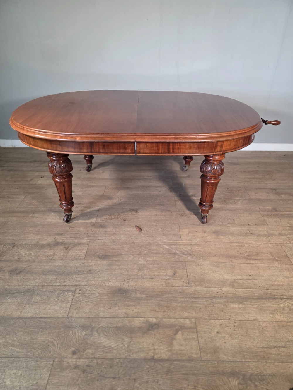 An antique Victorian mahogany extending dining table featuring an oval top, turned carved legs, and brass castors. View II