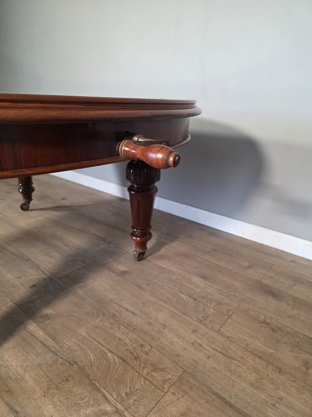 An antique Victorian mahogany extending dining table featuring an oval top, turned carved legs, and brass castors. View IV