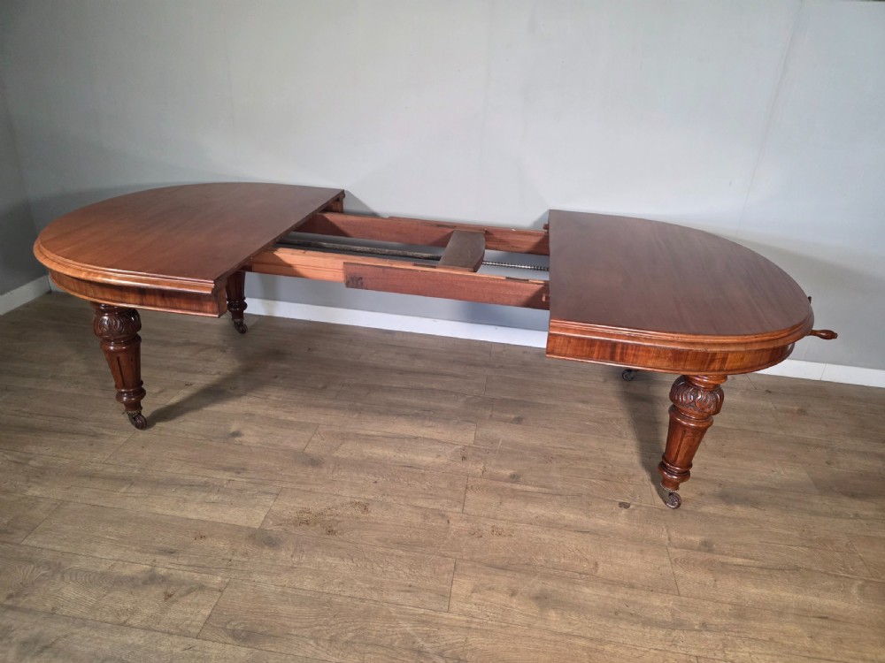 An antique Victorian mahogany extending dining table featuring an oval top, turned carved legs, and brass castors. View VI
