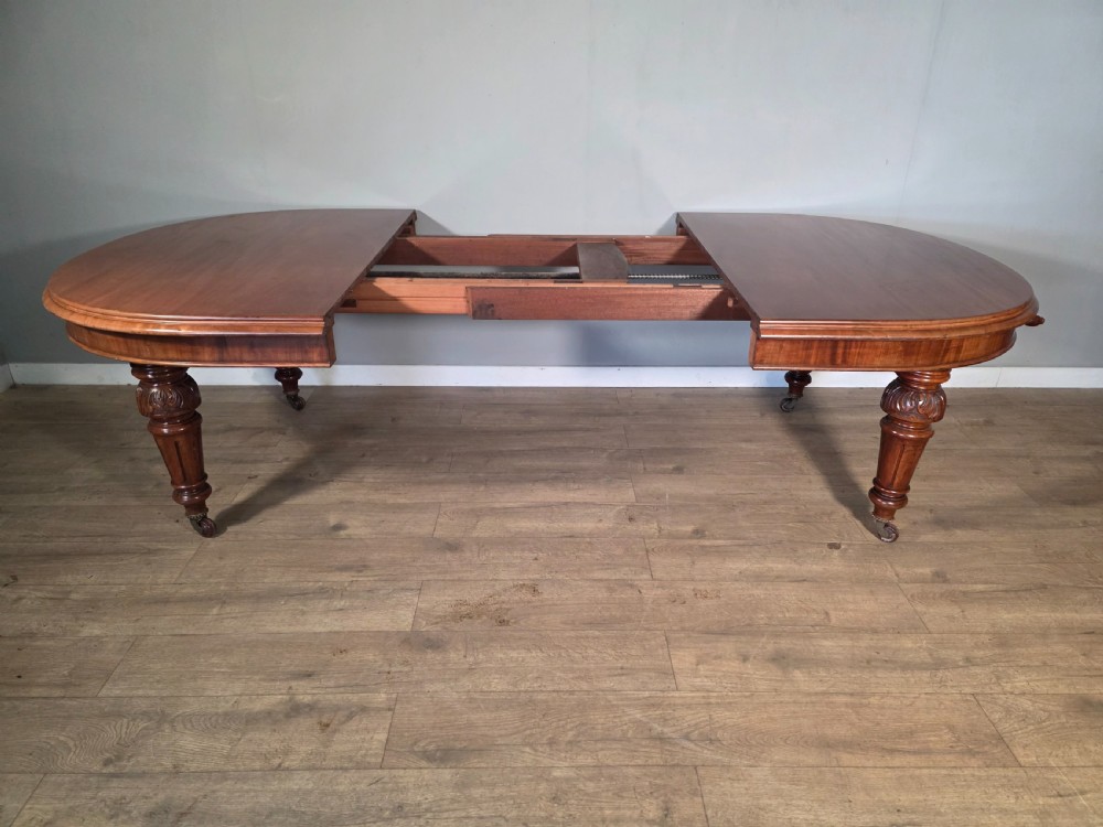 An antique Victorian mahogany extending dining table featuring an oval top, turned carved legs, and brass castors. View VII