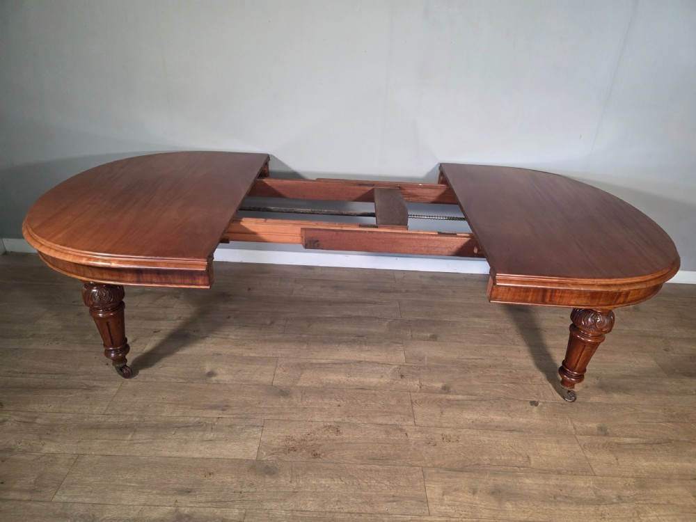An antique Victorian mahogany extending dining table featuring an oval top, turned carved legs, and brass castors. View VIII
