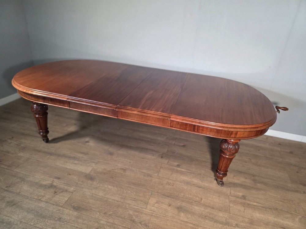 An antique Victorian mahogany extending dining table featuring an oval top, turned carved legs, and brass castors. View IX