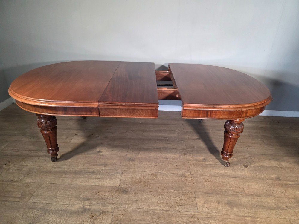 An antique Victorian mahogany extending dining table featuring an oval top, turned carved legs, and brass castors. View XIII