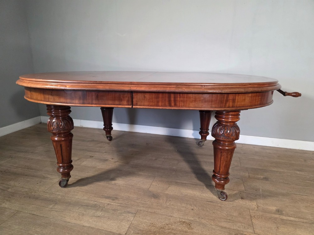 An antique Victorian mahogany extending dining table featuring an oval top, turned carved legs, and brass castors. View XIV