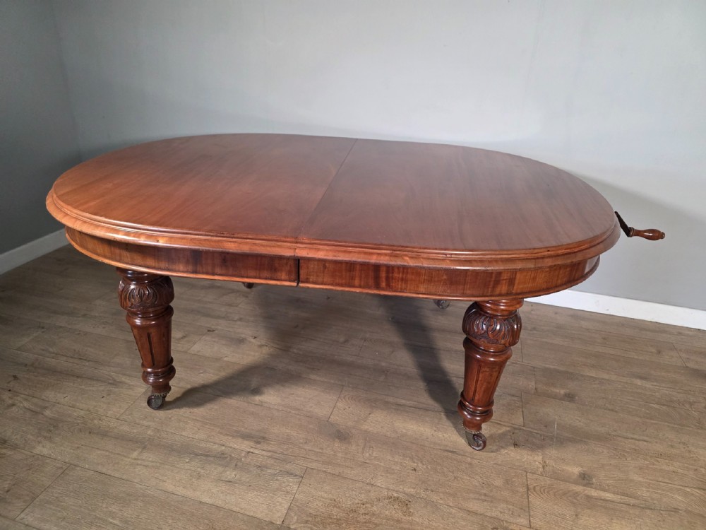 An antique Victorian mahogany extending dining table featuring an oval top, turned carved legs, and brass castors. View XV