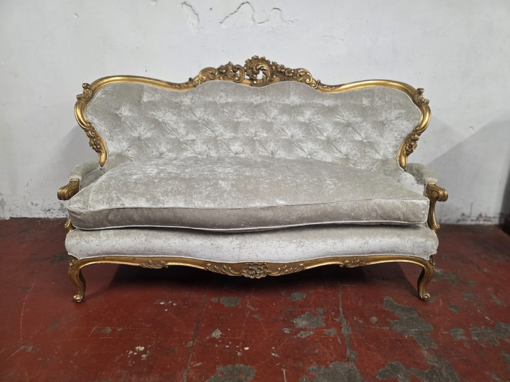 A late 19th-century Victorian Rococo Revival sofa with a carved gold giltwood frame, deep button-tufted light grey velvet backrest, and cabriole legs.