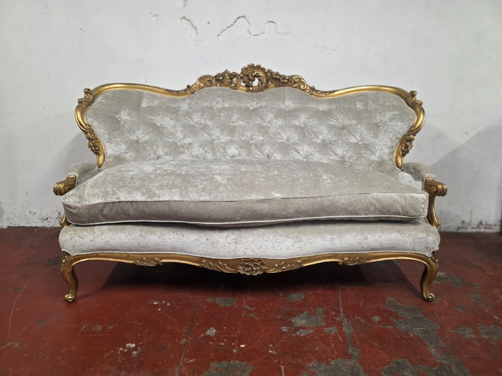 A late 19th-century Victorian Rococo Revival sofa with a carved gold giltwood frame, deep button-tufted light grey velvet backrest, and cabriole legs. View II