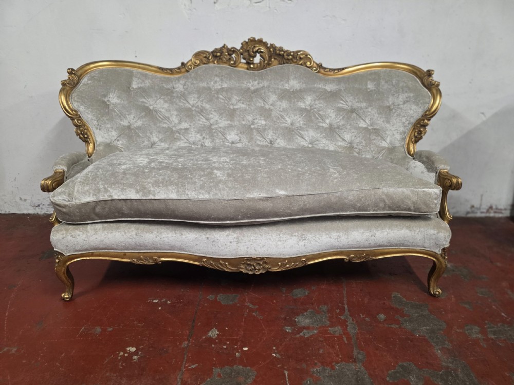 A late 19th-century Victorian Rococo Revival sofa with a carved gold giltwood frame, deep button-tufted light grey velvet backrest, and cabriole legs. View IV