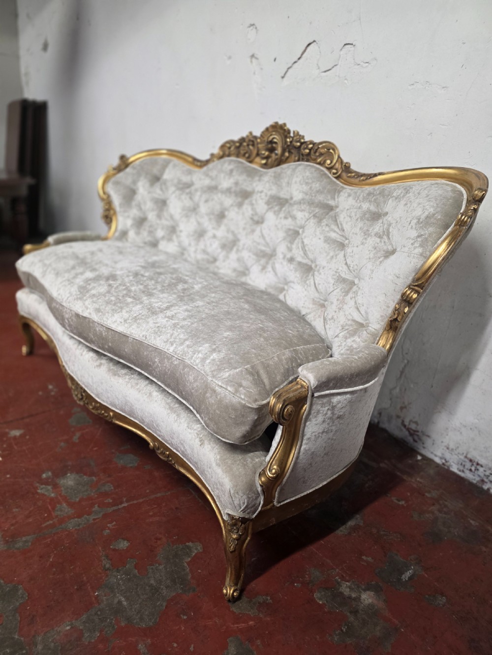 A late 19th-century Victorian Rococo Revival sofa with a carved gold giltwood frame, deep button-tufted light grey velvet backrest, and cabriole legs. View V