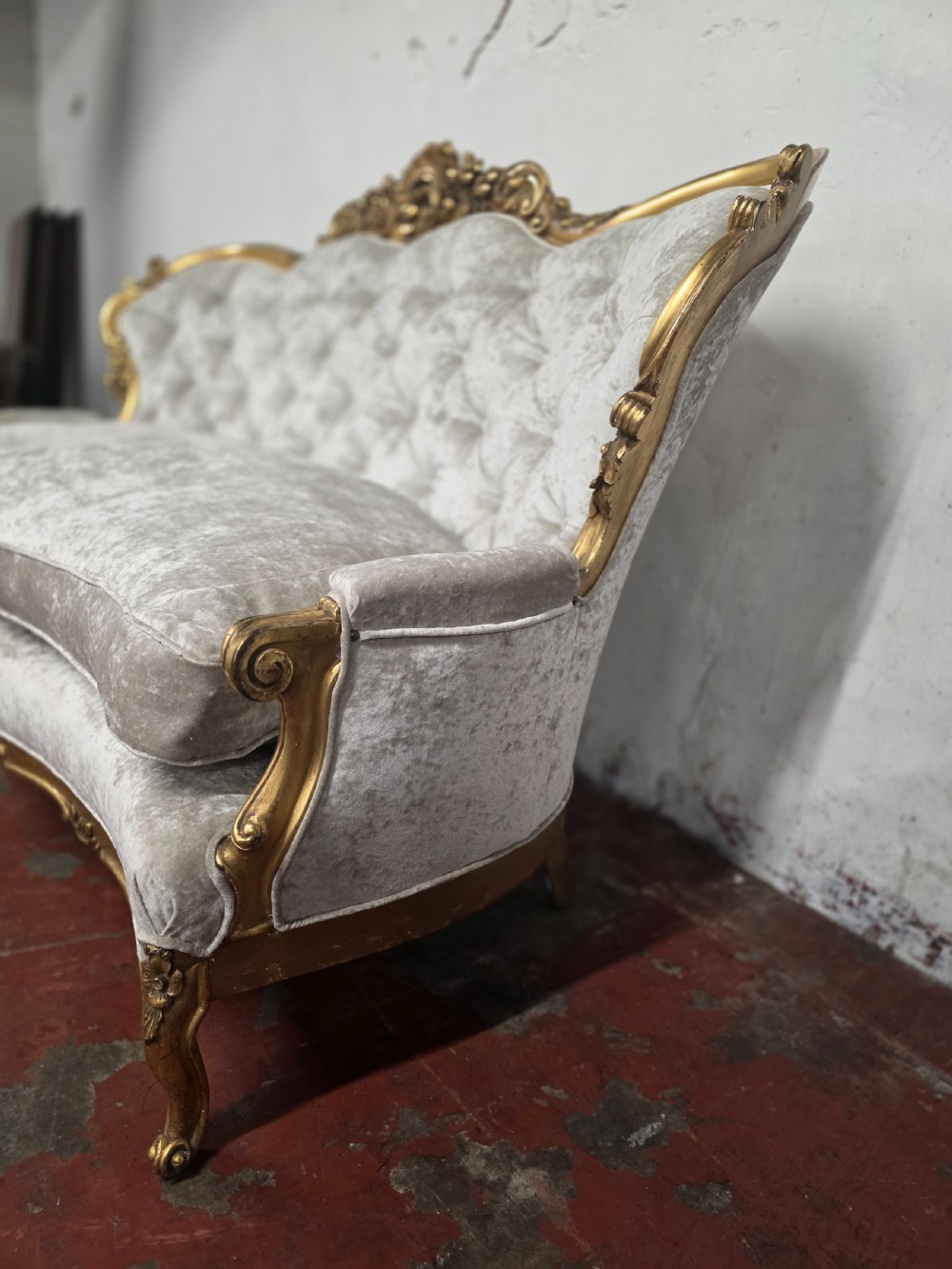 A late 19th-century Victorian Rococo Revival sofa with a carved gold giltwood frame, deep button-tufted light grey velvet backrest, and cabriole legs. View VI