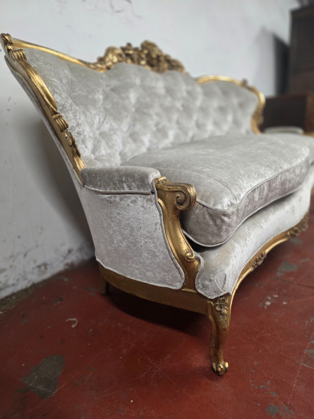 A late 19th-century Victorian Rococo Revival sofa with a carved gold giltwood frame, deep button-tufted light grey velvet backrest, and cabriole legs. View VII