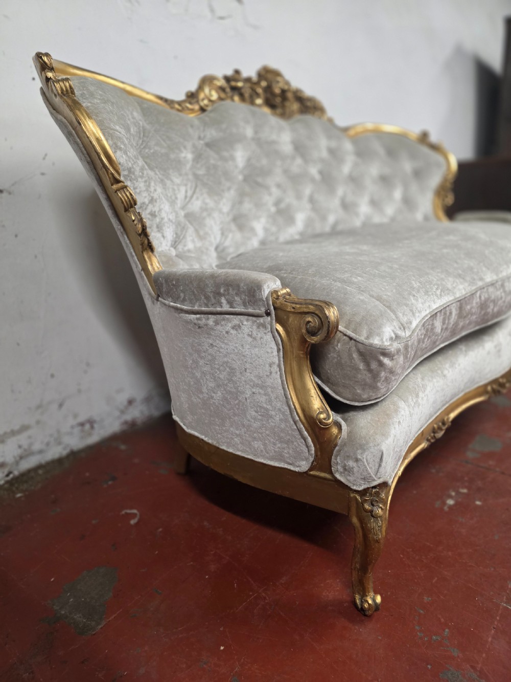 A late 19th-century Victorian Rococo Revival sofa with a carved gold giltwood frame, deep button-tufted light grey velvet backrest, and cabriole legs. View VIII