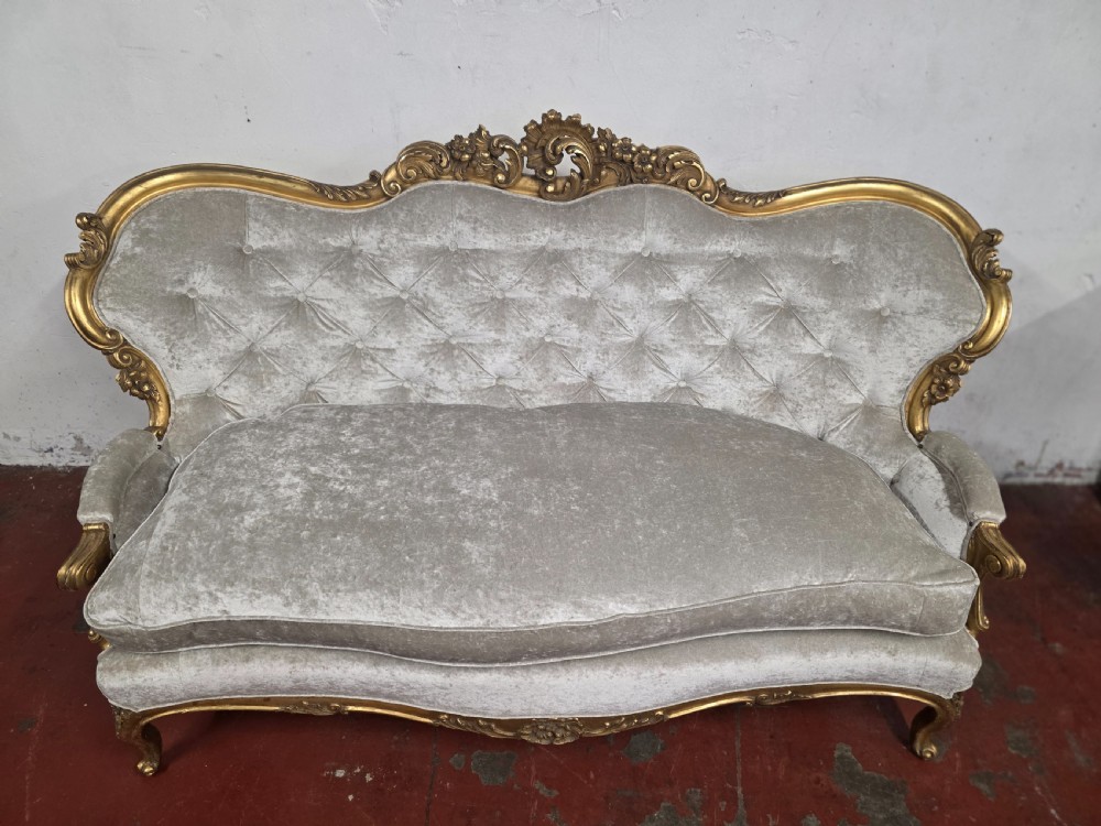 A late 19th-century Victorian Rococo Revival sofa with a carved gold giltwood frame, deep button-tufted light grey velvet backrest, and cabriole legs. View IX