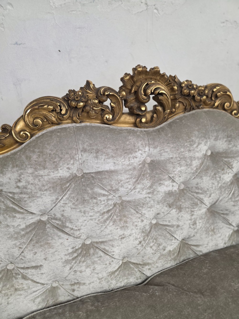 A late 19th-century Victorian Rococo Revival sofa with a carved gold giltwood frame, deep button-tufted light grey velvet backrest, and cabriole legs. View X