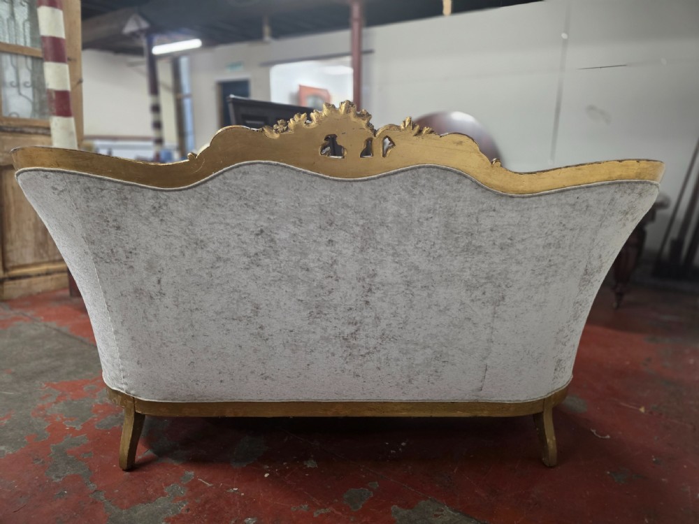 A late 19th-century Victorian Rococo Revival sofa with a carved gold giltwood frame, deep button-tufted light grey velvet backrest, and cabriole legs. View XIII