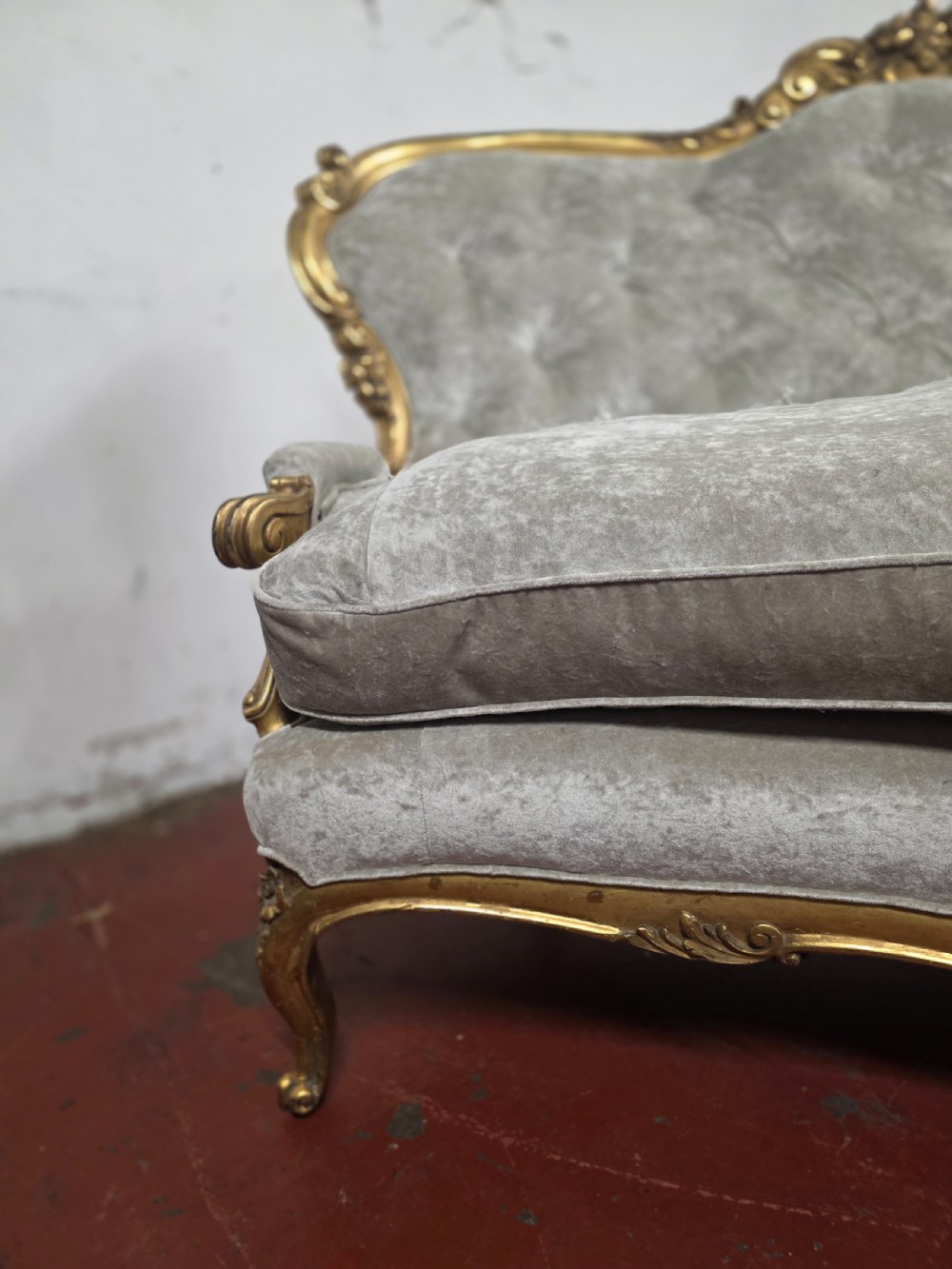 A late 19th-century Victorian Rococo Revival sofa with a carved gold giltwood frame, deep button-tufted light grey velvet backrest, and cabriole legs. View XV