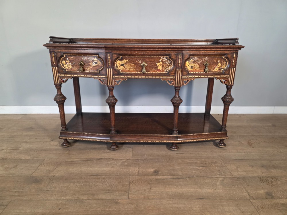 An antique solid oak console table featuring carved drawers, inlaid details, turned supports, and an undertier shelf.