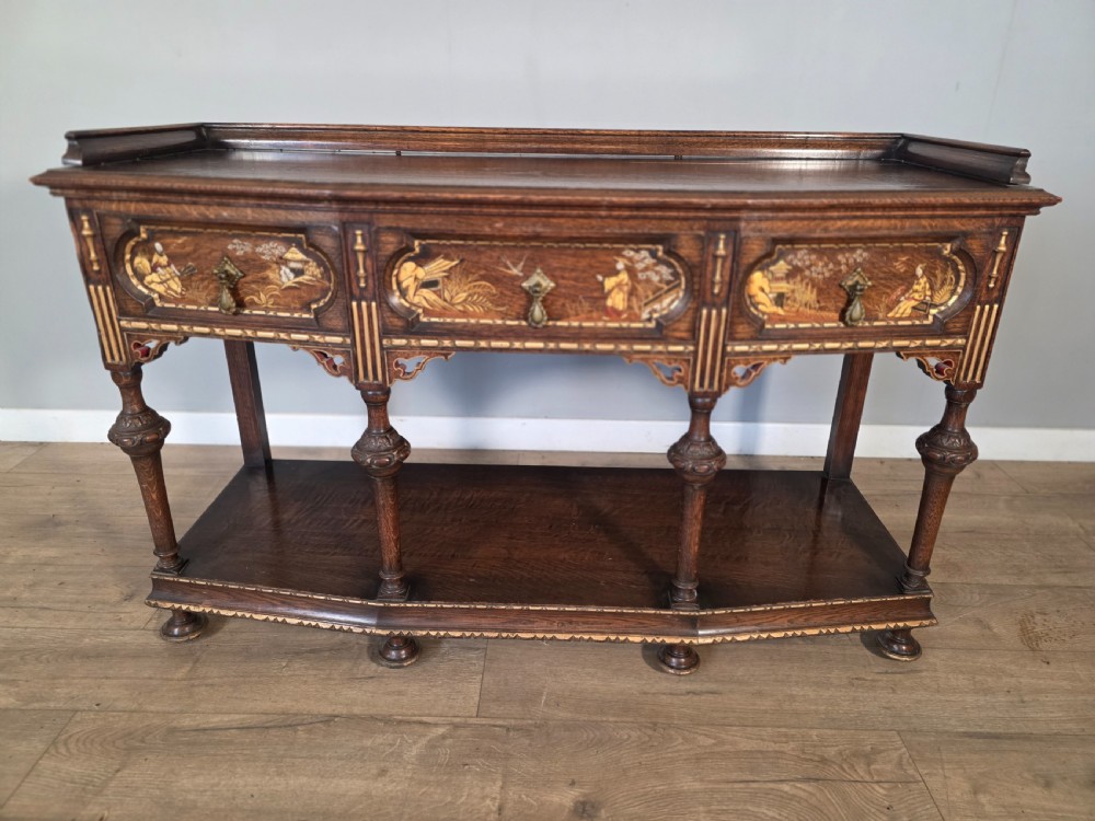 An antique solid oak console table featuring carved drawers, inlaid details, turned supports, and an undertier shelf. View V