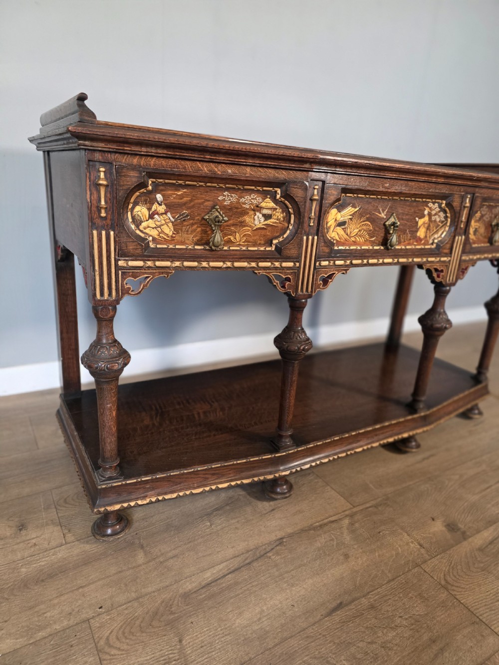 An antique solid oak console table featuring carved drawers, inlaid details, turned supports, and an undertier shelf. View VI