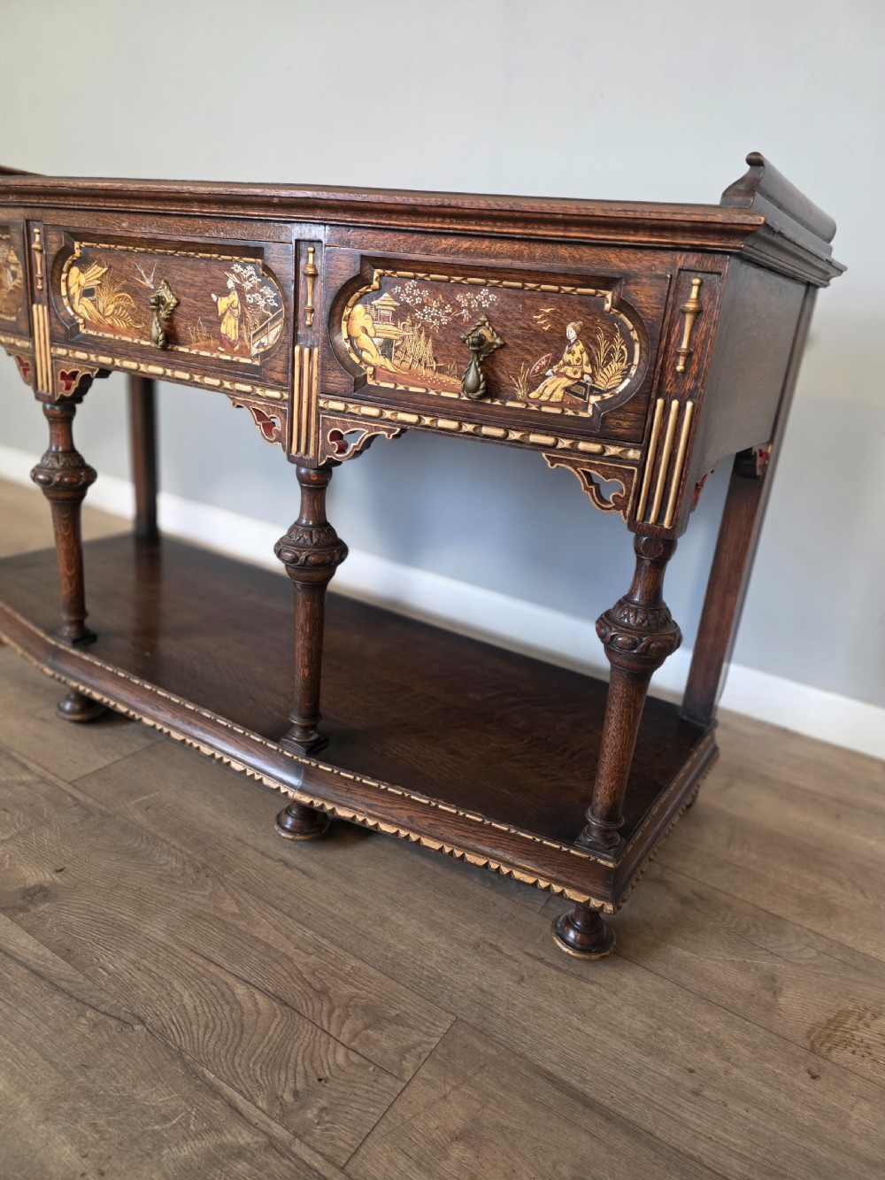 An antique solid oak console table featuring carved drawers, inlaid details, turned supports, and an undertier shelf. View VII