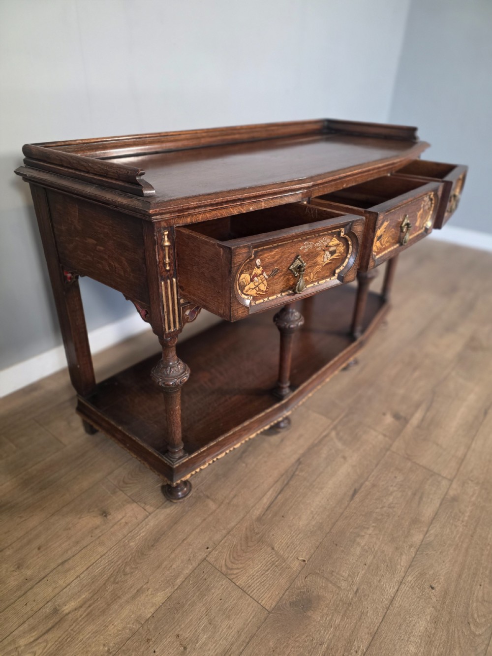 An antique solid oak console table featuring carved drawers, inlaid details, turned supports, and an undertier shelf. View IX