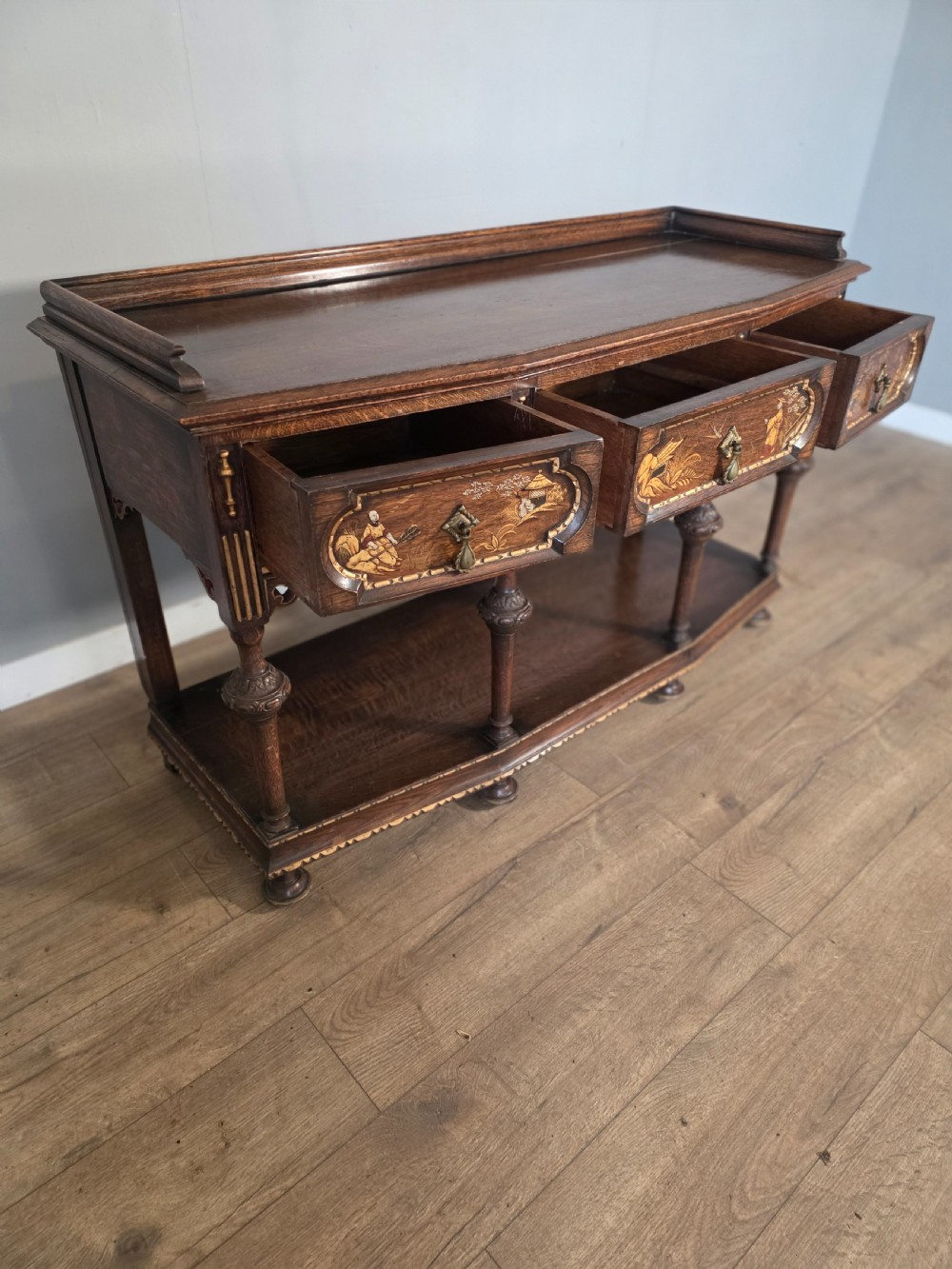 An antique solid oak console table featuring carved drawers, inlaid details, turned supports, and an undertier shelf. View X