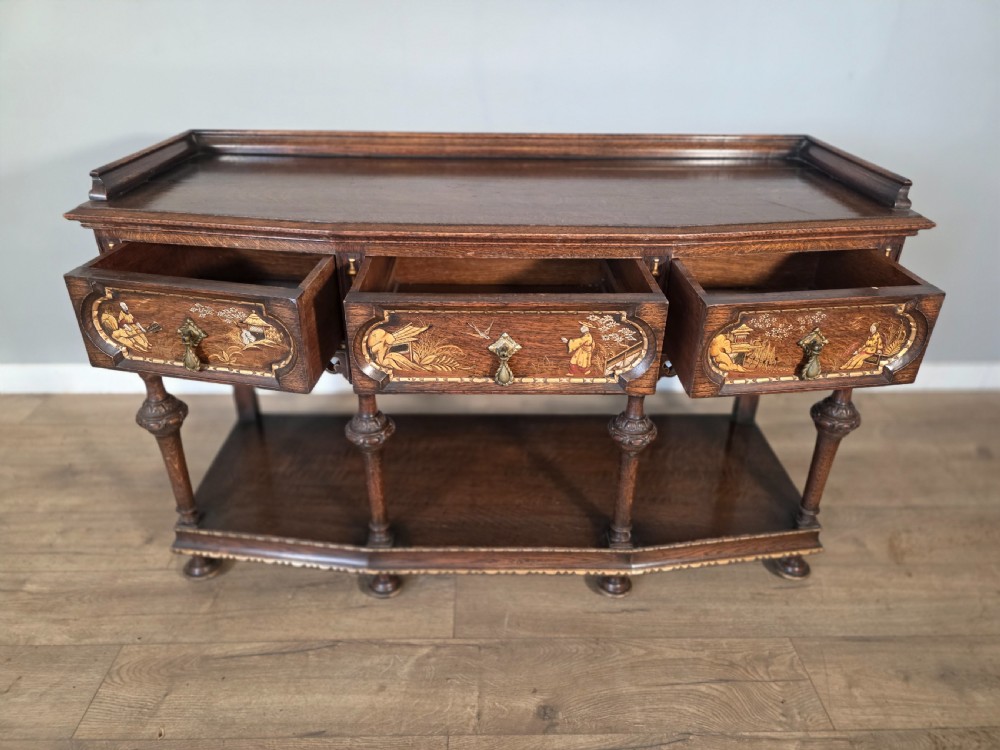 An antique solid oak console table featuring carved drawers, inlaid details, turned supports, and an undertier shelf. View XI