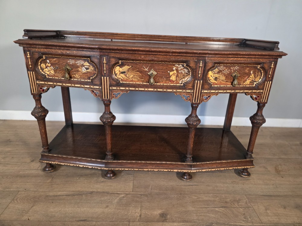 An antique solid oak console table featuring carved drawers, inlaid details, turned supports, and an undertier shelf. View XVI