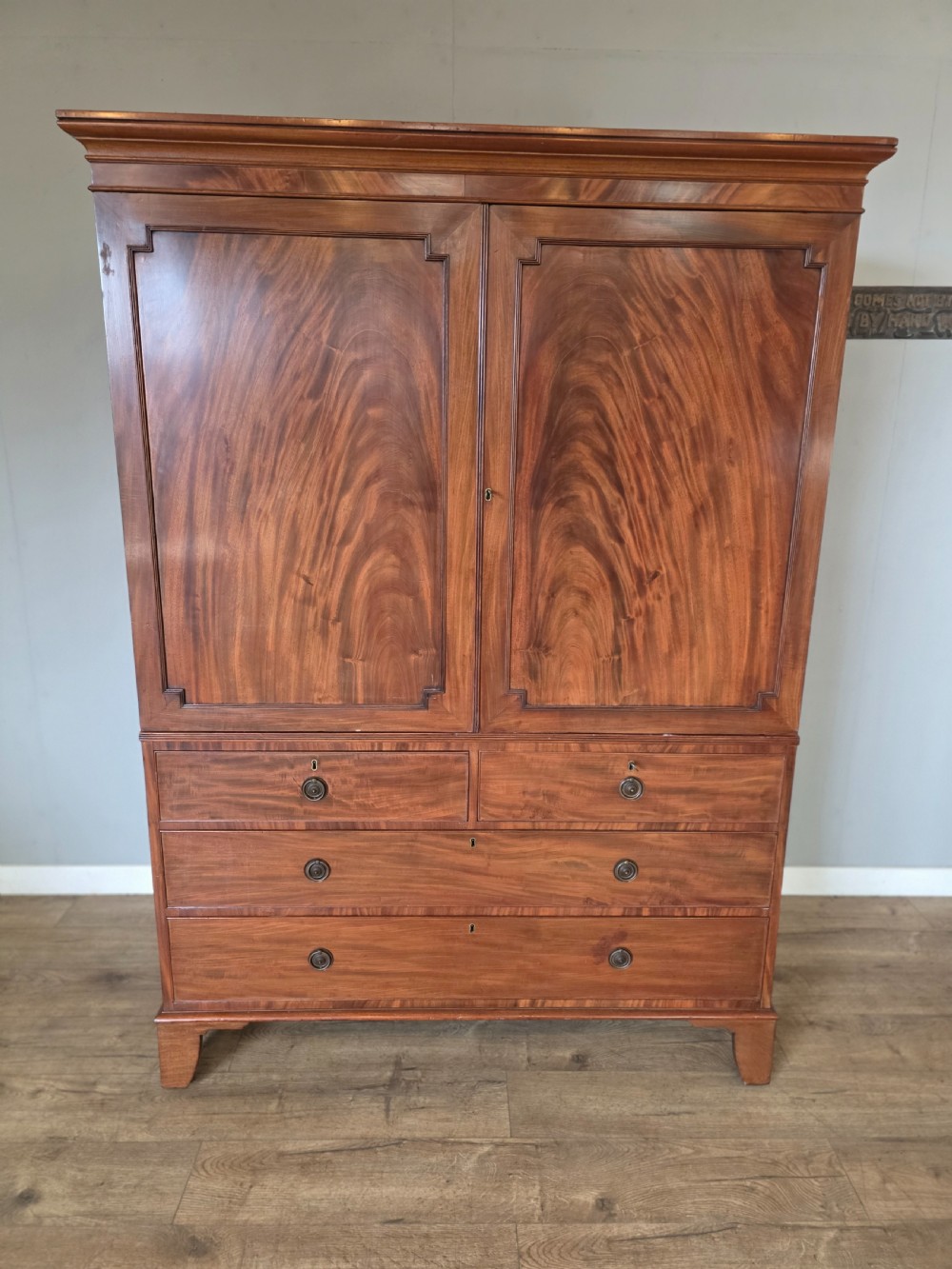 A George III mahogany linen press featuring flame mahogany panelled cupboard doors above a base of four drawers.