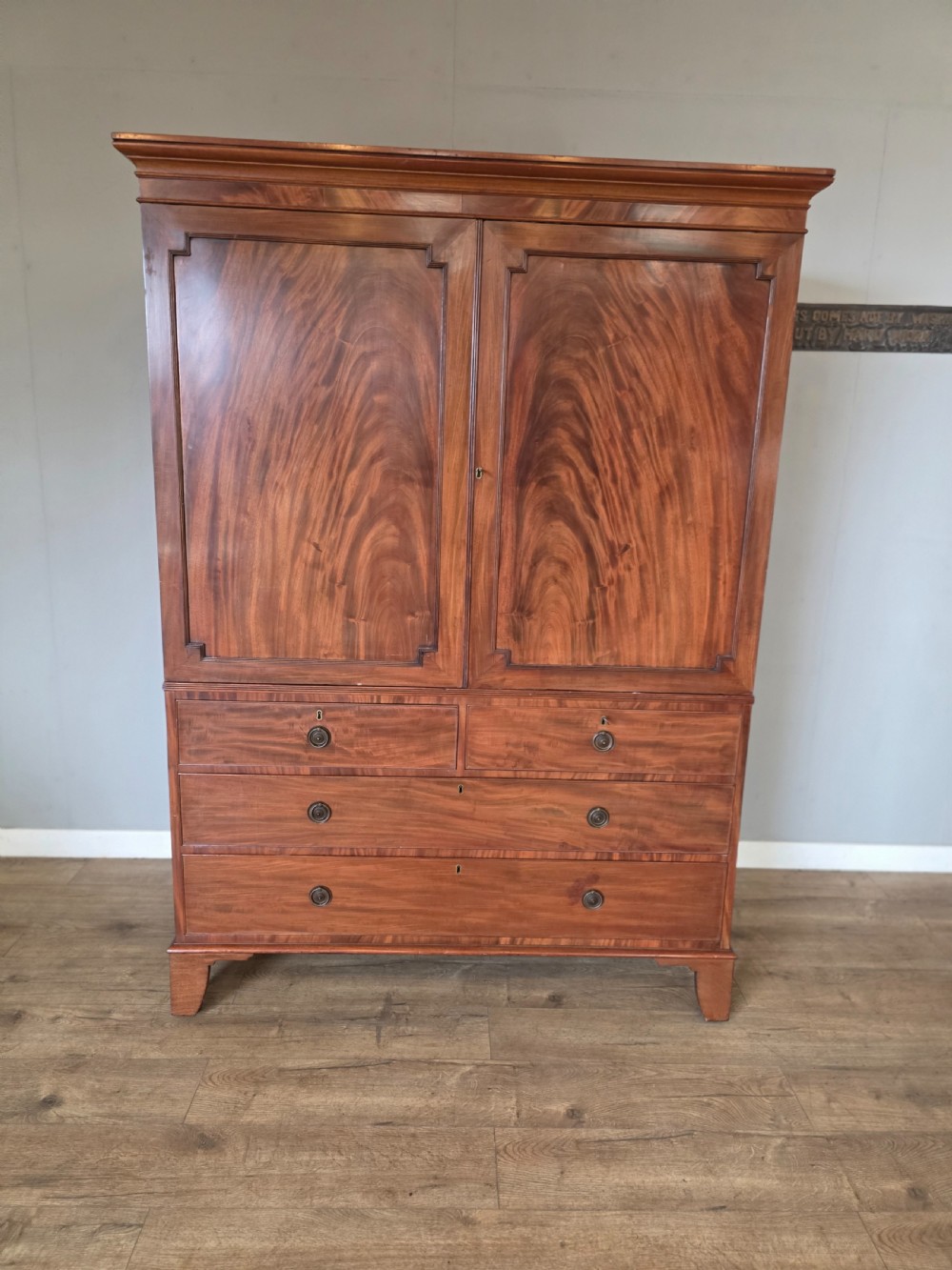 A George III mahogany linen press featuring flame mahogany panelled cupboard doors above a base of four drawers. View II