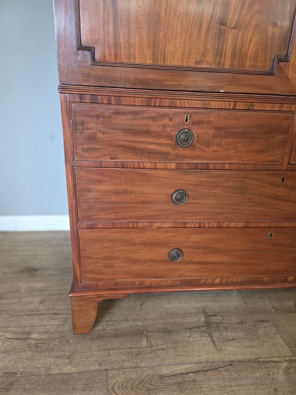 A George III mahogany linen press featuring flame mahogany panelled cupboard doors above a base of four drawers. View III
