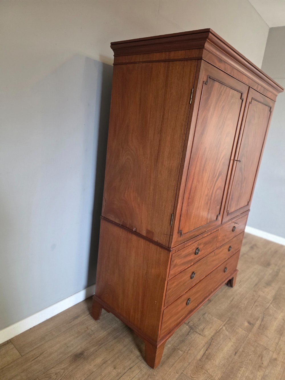 A George III mahogany linen press featuring flame mahogany panelled cupboard doors above a base of four drawers. View IV