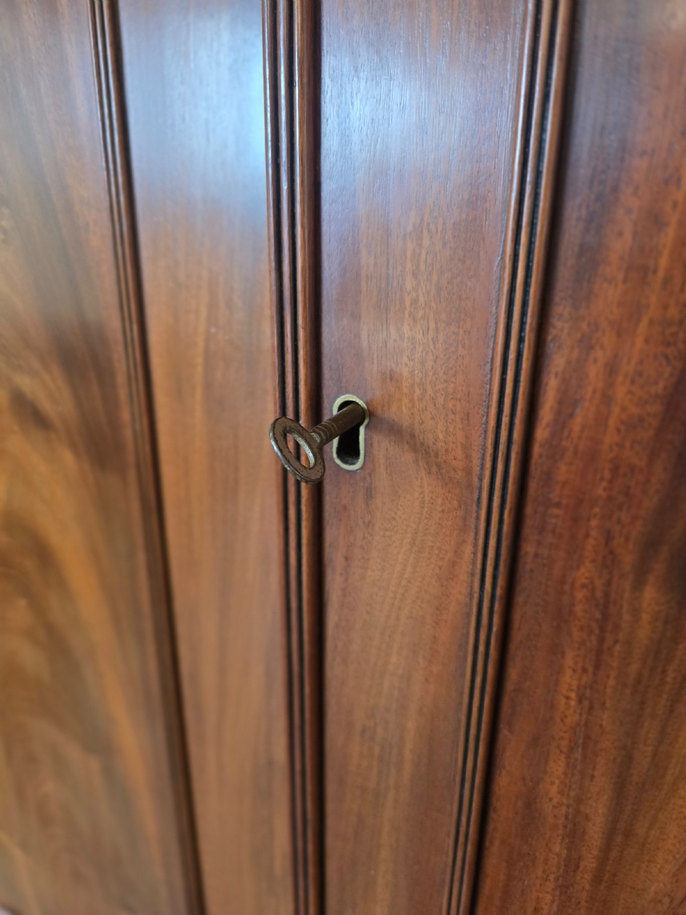 A George III mahogany linen press featuring flame mahogany panelled cupboard doors above a base of four drawers. View V