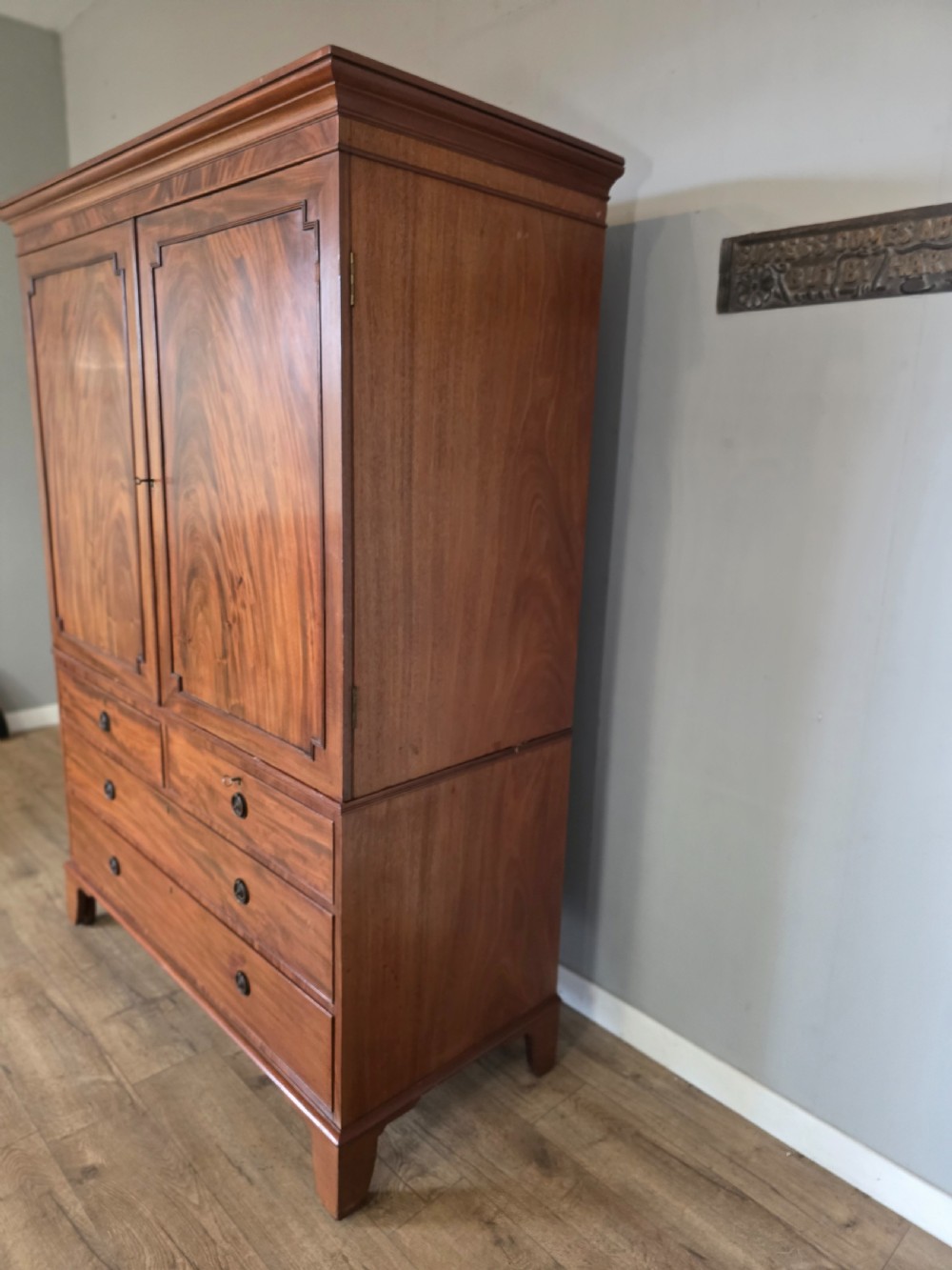 A George III mahogany linen press featuring flame mahogany panelled cupboard doors above a base of four drawers. View VI