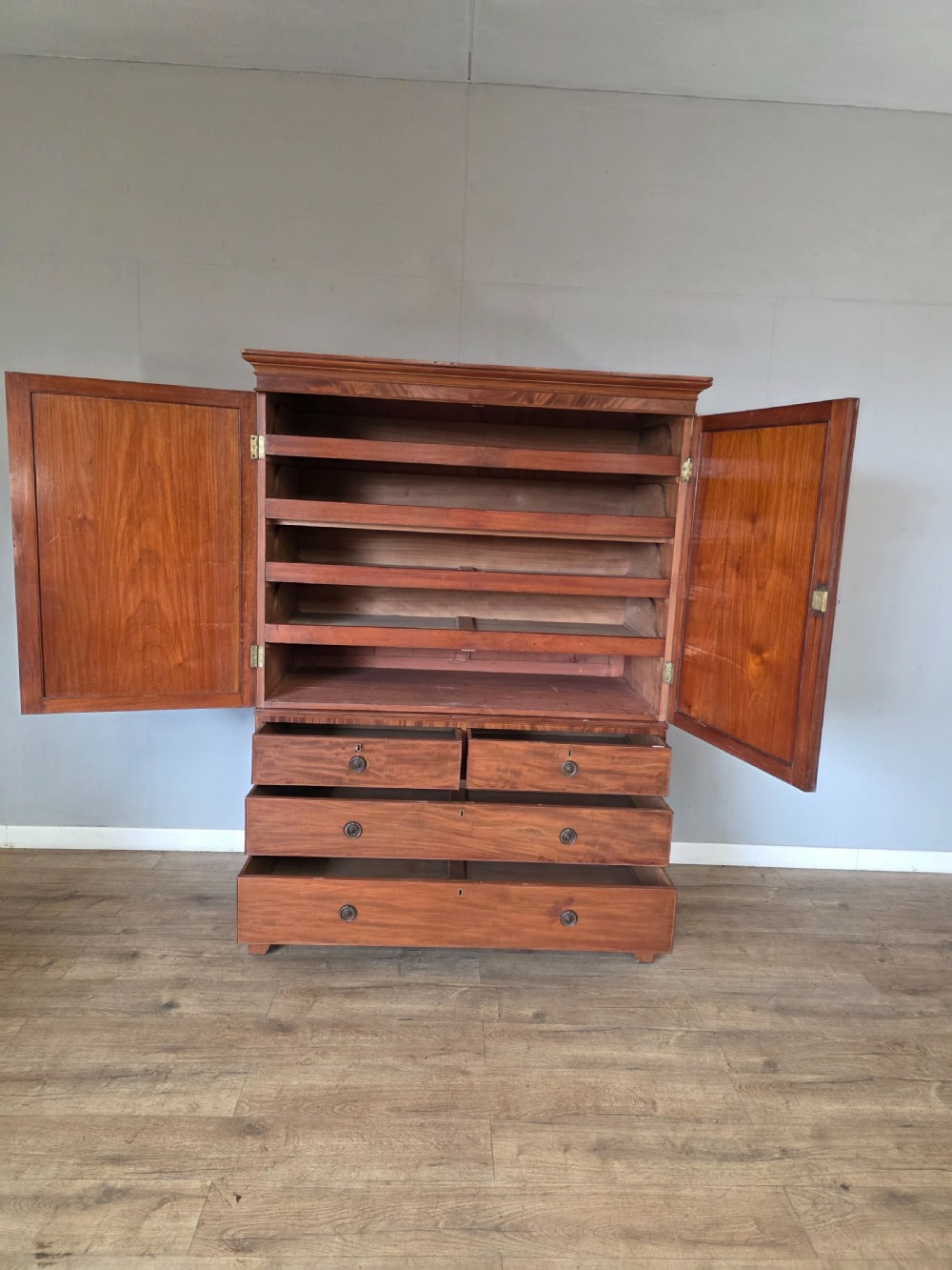A George III mahogany linen press featuring flame mahogany panelled cupboard doors above a base of four drawers. View VII