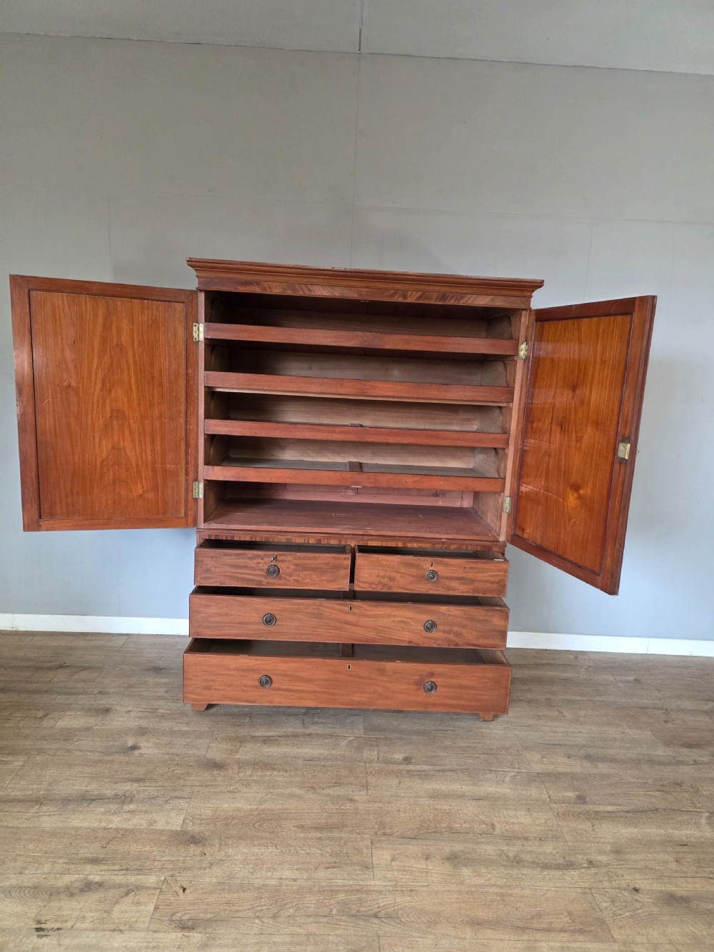 A George III mahogany linen press featuring flame mahogany panelled cupboard doors above a base of four drawers. View VIII