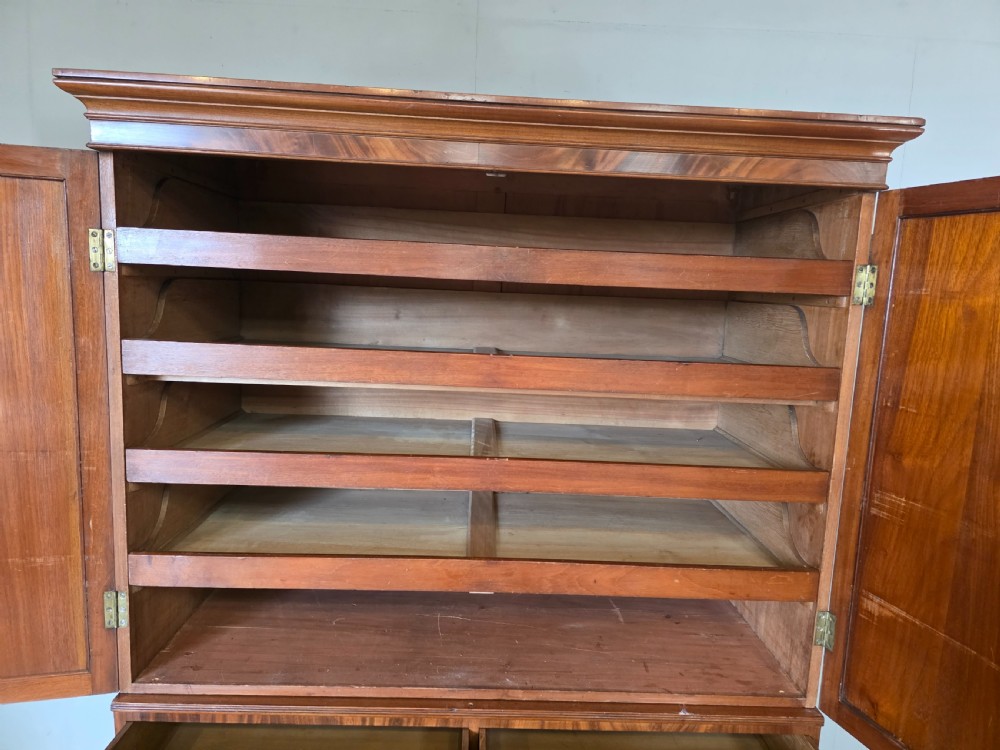 A George III mahogany linen press featuring flame mahogany panelled cupboard doors above a base of four drawers. View X
