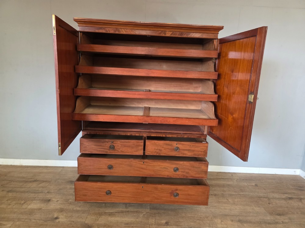 A George III mahogany linen press featuring flame mahogany panelled cupboard doors above a base of four drawers. View XI