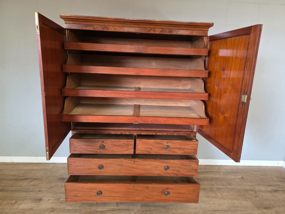 A George III mahogany linen press featuring flame mahogany panelled cupboard doors above a base of four drawers. View XII