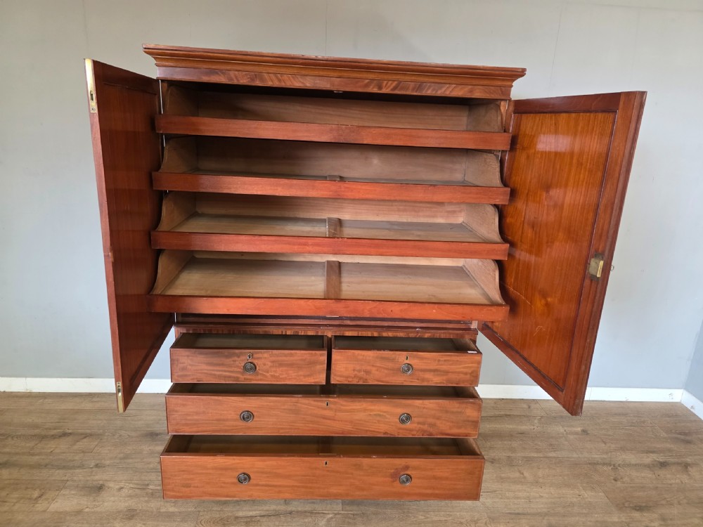 A George III mahogany linen press featuring flame mahogany panelled cupboard doors above a base of four drawers. View XIII