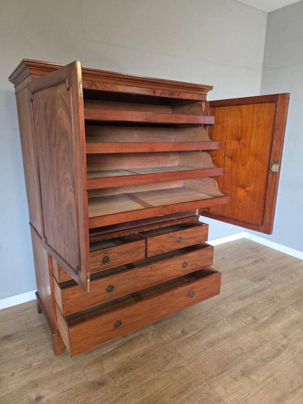 A George III mahogany linen press featuring flame mahogany panelled cupboard doors above a base of four drawers. View XIV