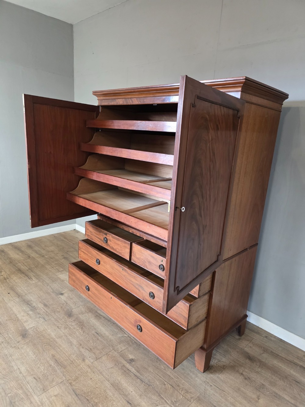 A George III mahogany linen press featuring flame mahogany panelled cupboard doors above a base of four drawers. View XV