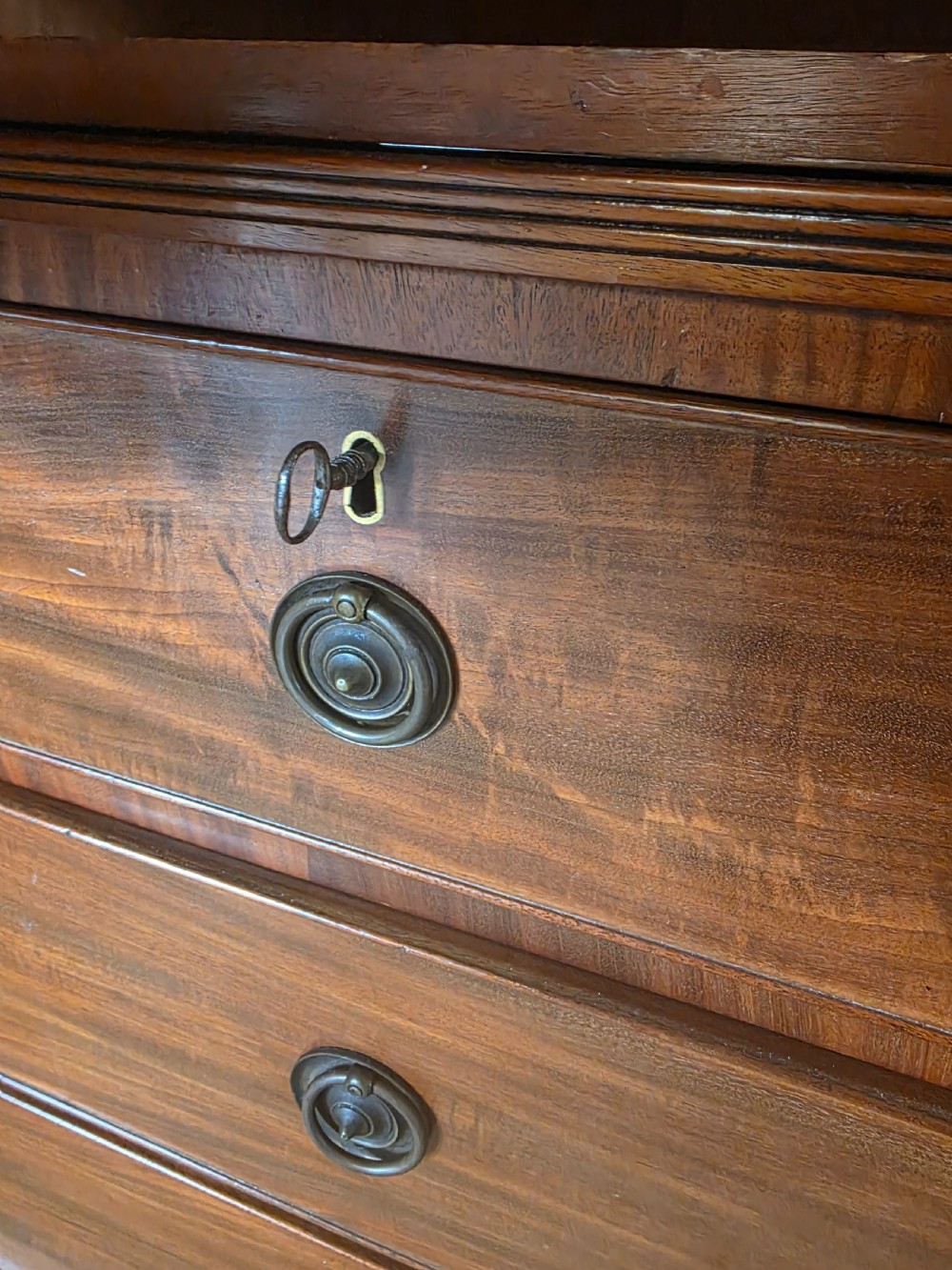A George III mahogany linen press featuring flame mahogany panelled cupboard doors above a base of four drawers. View XVI