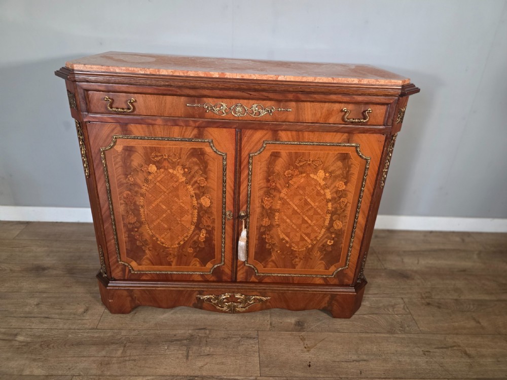 A 1920s French wooden cupboard featuring intricate floral marquetry inlay, gilt metal mounts, a single top drawer, two cabinet doors, and a reddish marble top surface. View II