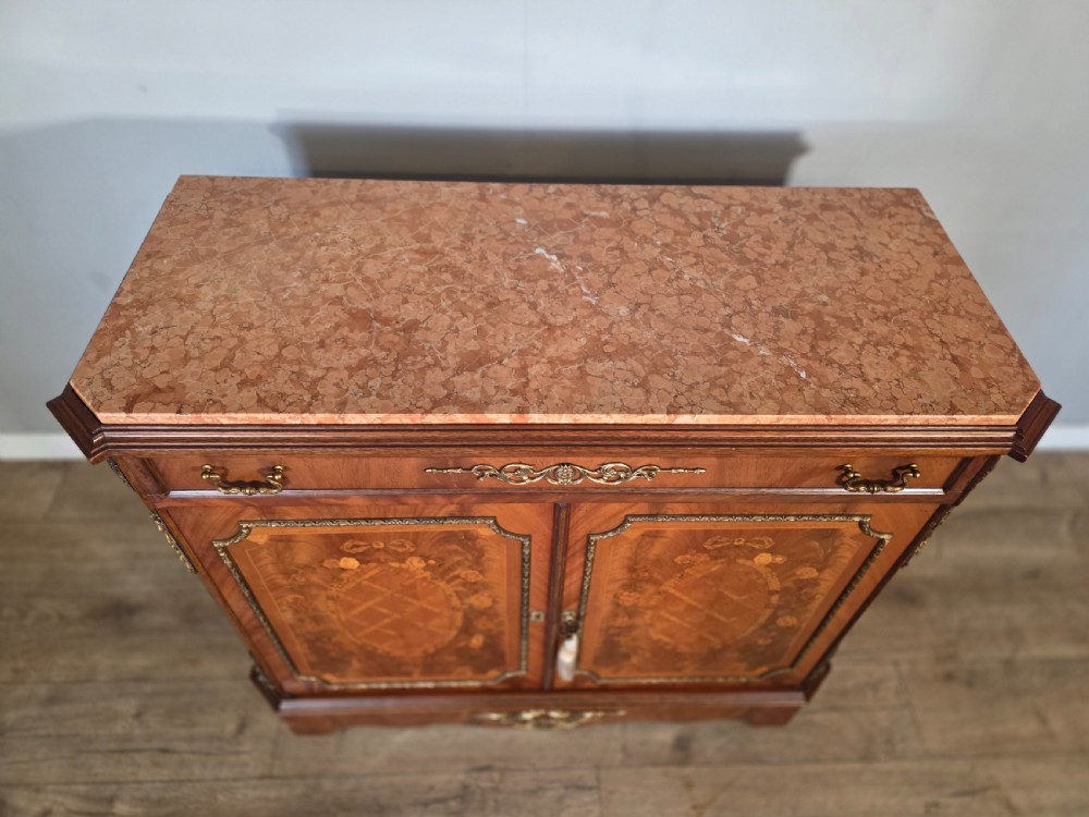 A 1920s French wooden cupboard featuring intricate floral marquetry inlay, gilt metal mounts, a single top drawer, two cabinet doors, and a reddish marble top surface. View V