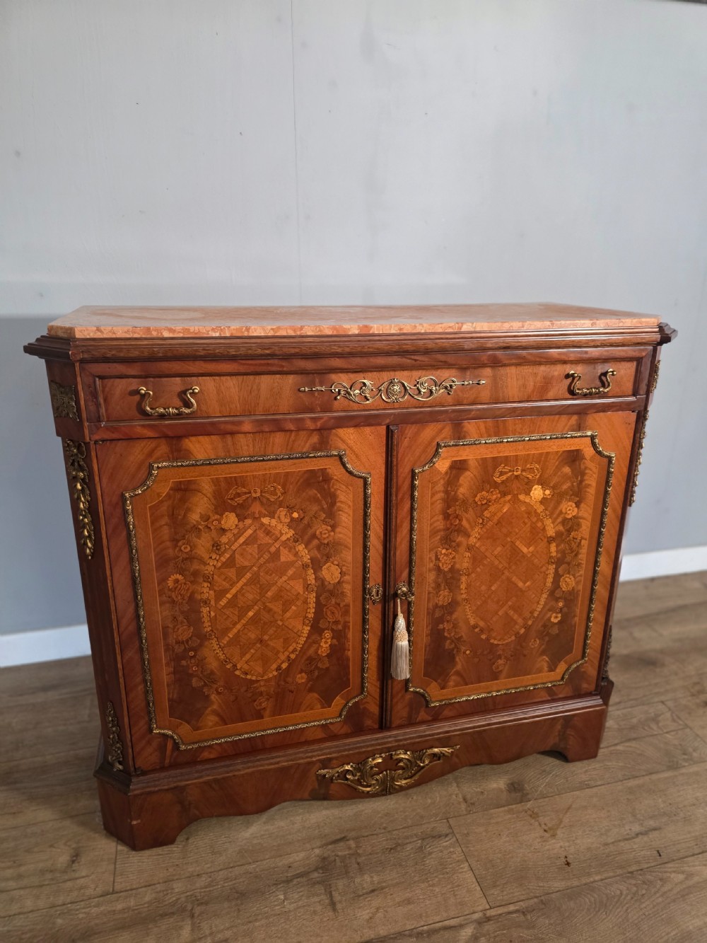 A 1920s French wooden cupboard featuring intricate floral marquetry inlay, gilt metal mounts, a single top drawer, two cabinet doors, and a reddish marble top surface. View XII