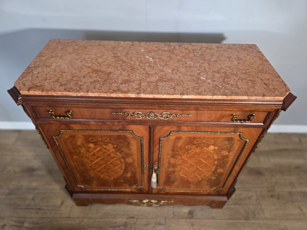 A 1920s French wooden cupboard featuring intricate floral marquetry inlay, gilt metal mounts, a single top drawer, two cabinet doors, and a reddish marble top surface. View XV