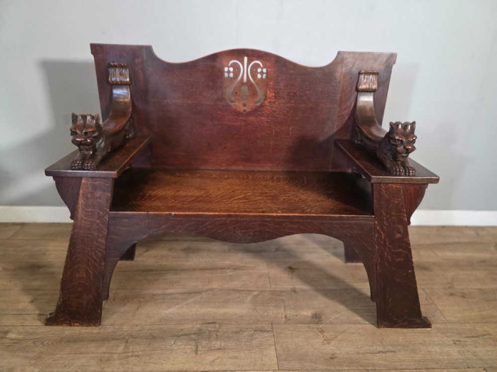 A dark oak Arts and Crafts hall bench featuring carved lion armrests, angled side legs, and a stylized inlaid motif on the backrest. View II