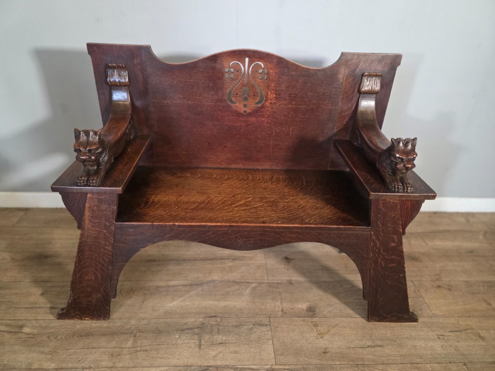 A dark oak Arts and Crafts hall bench featuring carved lion armrests, angled side legs, and a stylized inlaid motif on the backrest. View III